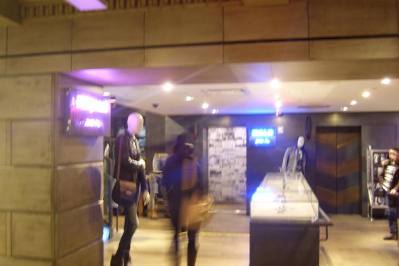 Image of the inside of a department store. A pink neon sign on the left says "Female" and "2nd floor" and a blue neon sign on the right says "Male" and "3rd floor"